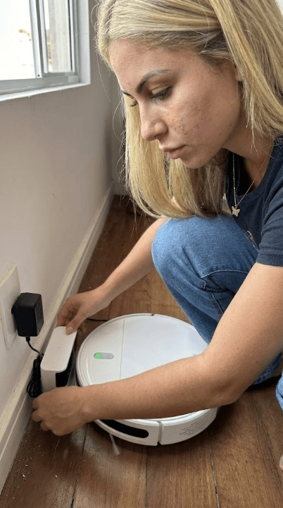Isabelle ligando o robô aspirador na tomada da sala