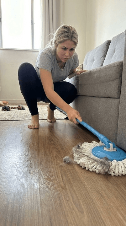 Isa limpando embaixo do sofá e mostrando a centrífuga secando o mop